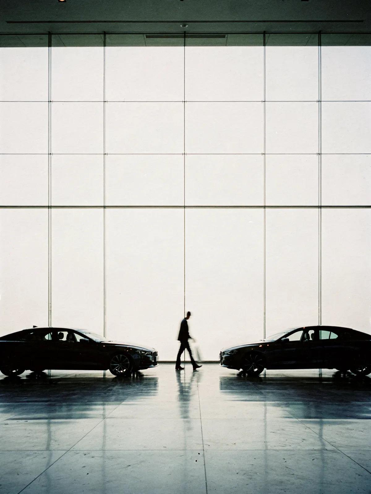 Autohaus-Ausstellungsraum hinter einer hohen Glasfront im Gegenlicht, davor Fahrzeuge als dunkle Silhouetten, KI-generiert