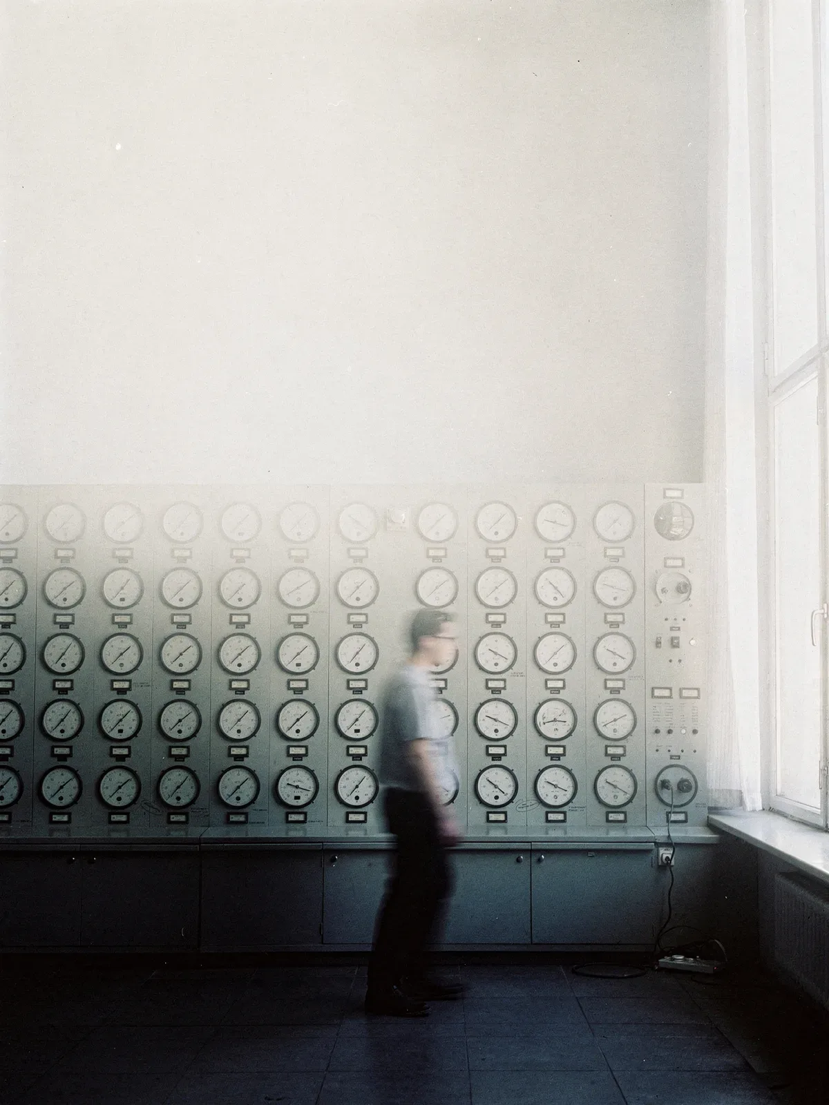 Heller Messraum mit einer Wand aus analogen Zeigerinstrumenten, eine Person geht bewegungsunscharf vorbei, KI-generiert