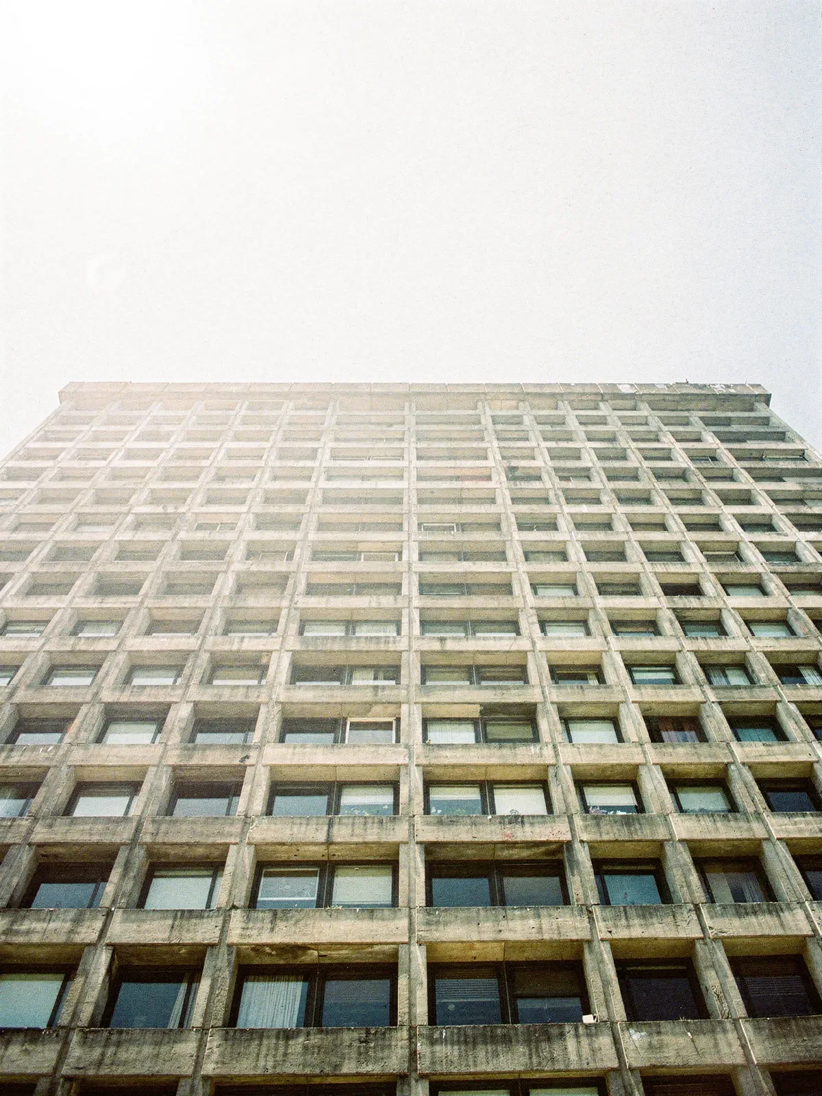 Betonfassade mit strengem Fensterraster gegen hellen Himmel, harte Schatten, KI-generiert