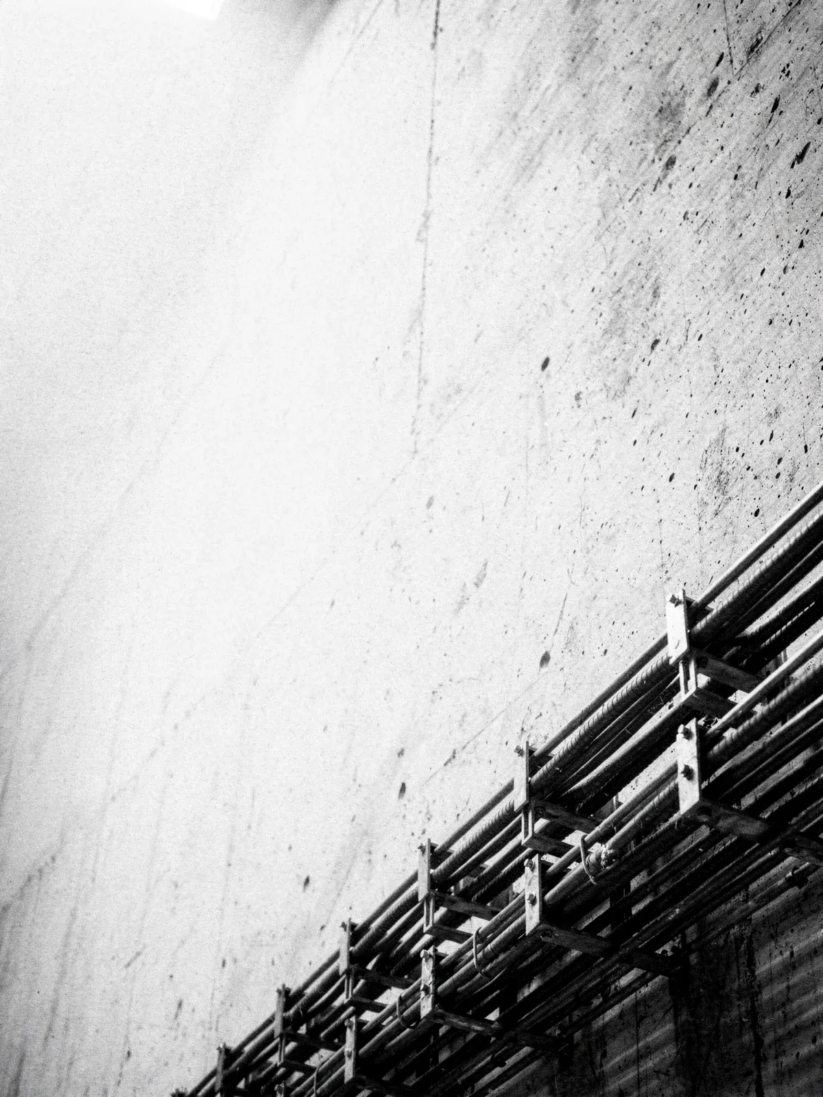 Kabeltrasse mit parallel geführten Leitungen an einer hellen Betonwand, daneben eine große helle Leerfläche, KI-generiert