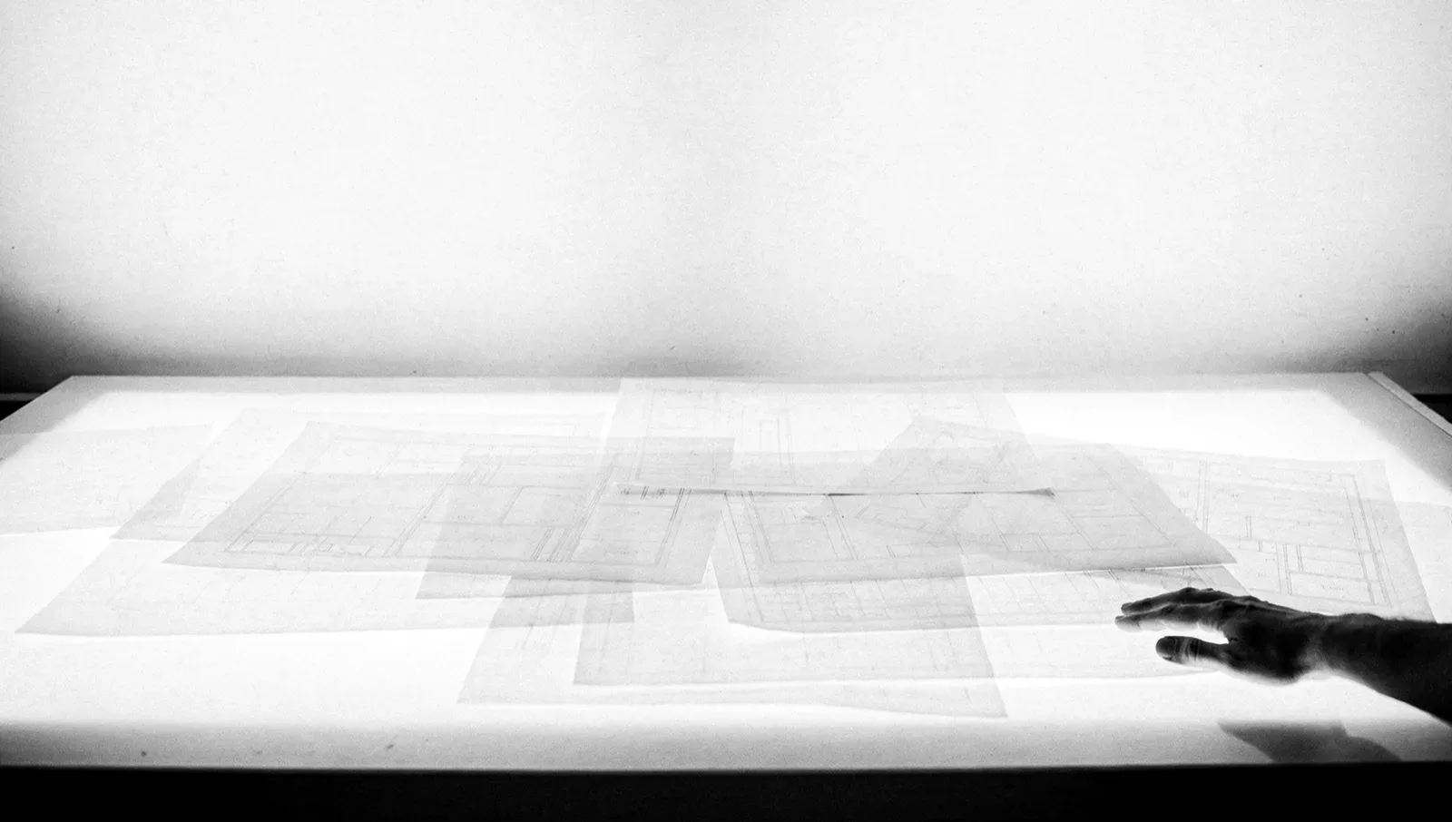 Übereinanderliegende Transparentpapiere mit Layoutrastern auf einem durchleuchteten Tisch, KI-generiert